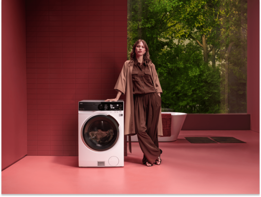 Woman standing next to washing machine.